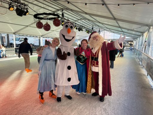 Groep mensen in kostuums, inclusief Olaf, een prinses en de kerstman, op een schaatsbaan.