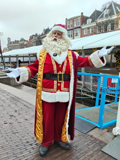 Kerstman in een rood pak met gouden details staat op een kade.